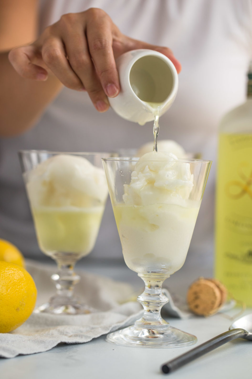 A woman's hand pouring a shot of limoncello over lemon sorbetto to make sgroppino al limone.