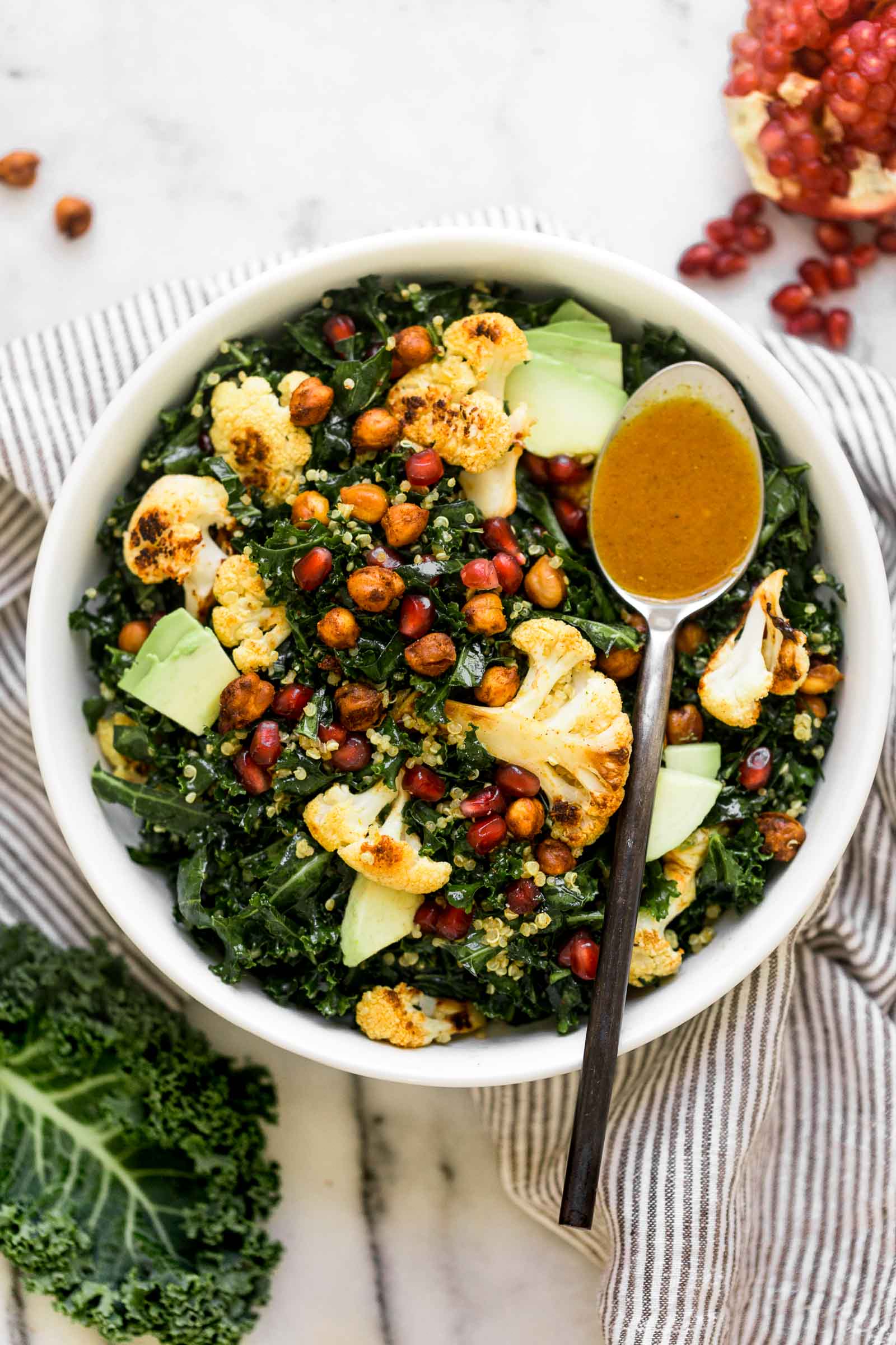 a nourishing & filling winter salad, this winter glow bowl is loaded with the best feel-good winter ingredients: roasted cauliflower, pomegranate arils, avocado, & kale, which all get tossed together in a homemade curry vinaigrette with spiced roasted chickpeas. winter salads have never looked this good! #salad #mealprep #saladrecipe #kalesalad #curryvinaigrette #roastedcauliflower #roastedchickpeas #playswellwithbutter