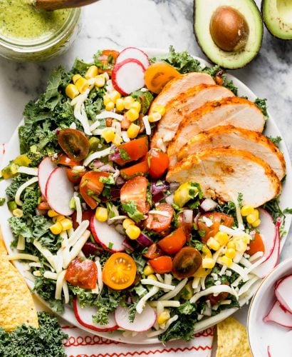 a healthy kale taco salad with chipotle lime chicken, roasted jalapeno vinaigrette, black beans, corn, pepper jack cheese, and a quick pico de gallo. this lightened-up take on a taco salad will be your new favorite! #playswellwithbutter #healthyrecipe #mealprep #healthyrecipe #kale #tacosalad #saladrecipe