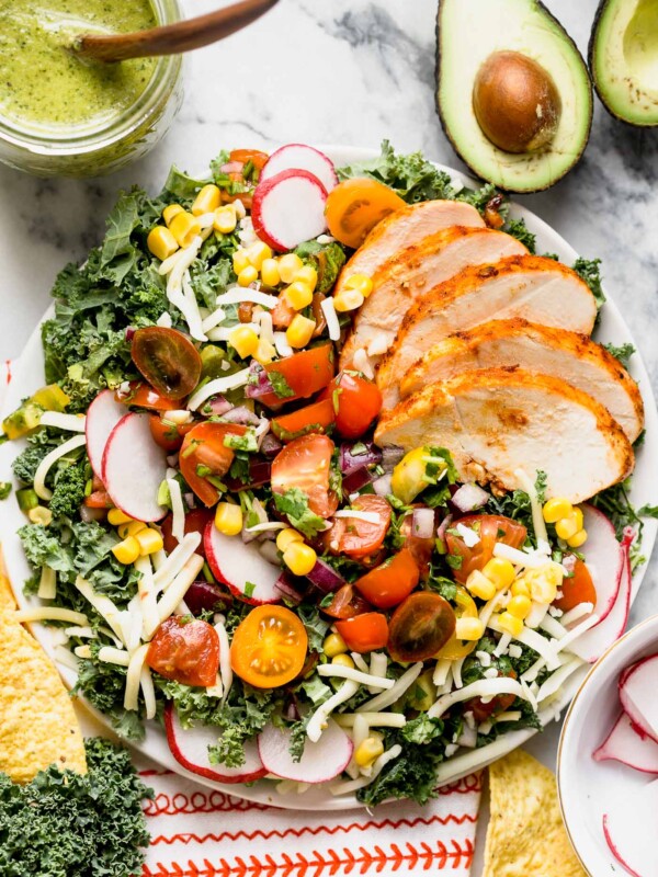 a healthy kale taco salad with chipotle lime chicken, roasted jalapeno vinaigrette, black beans, corn, pepper jack cheese, and a quick pico de gallo. this lightened-up take on a taco salad will be your new favorite! #playswellwithbutter #healthyrecipe #mealprep #healthyrecipe #kale #tacosalad #saladrecipe