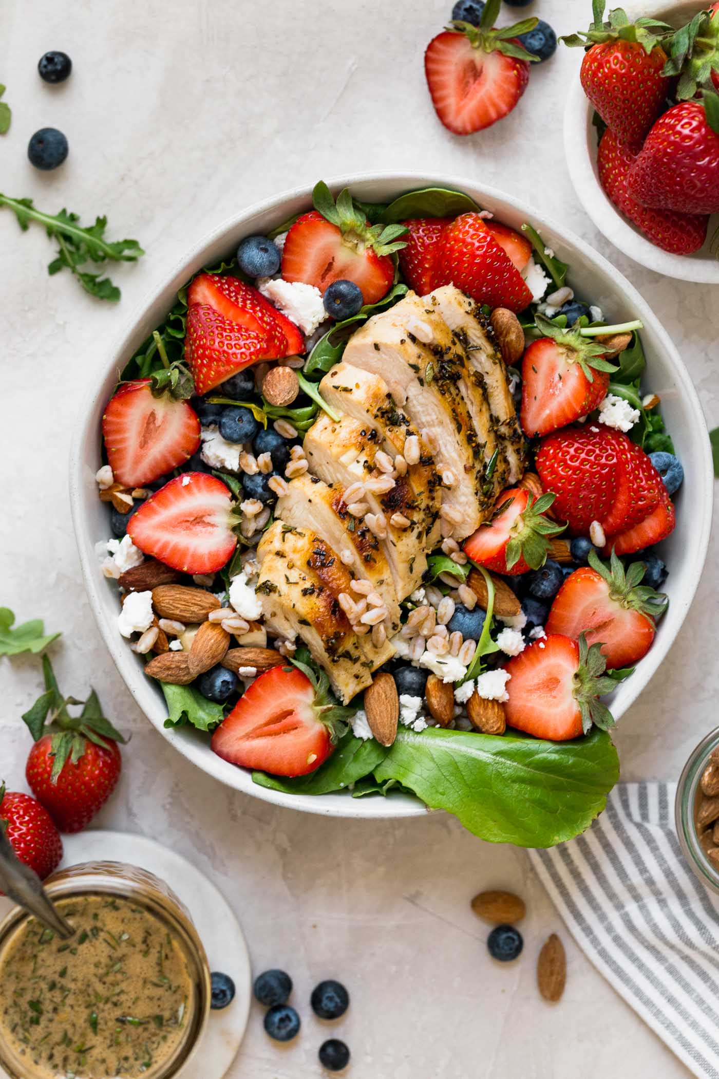 an easy & healthy strawberry salad just in time for spring!!! this strawberry salad is loaded with sweet strawberries & blueberries, tangy goat cheese, chopped almonds, farro, and gets topped with simple grilled chicken breast and drizzles of the most amazing homemade maple balsamic vinaigrette. the perfect healthy salad for meal prep, an easy weeknight dinner, or for summer entertaining! #playswellwithbutter #saladrecipe #strawberrysalad #healthyrecipe #lowcarbrecipe #balsamicvinaigrette