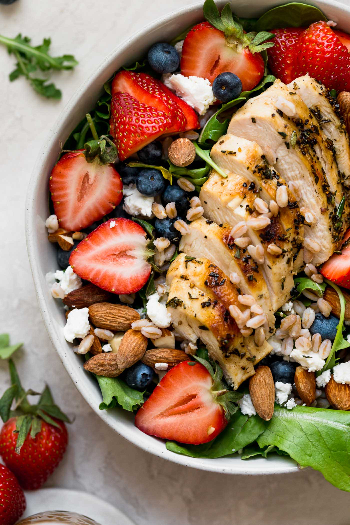 an easy & healthy strawberry salad just in time for spring!!! this strawberry salad is loaded with sweet strawberries & blueberries, tangy goat cheese, chopped almonds, farro, and gets topped with simple grilled chicken breast and drizzles of the most amazing homemade maple balsamic vinaigrette. the perfect healthy salad for meal prep, an easy weeknight dinner, or for summer entertaining! #playswellwithbutter #saladrecipe #strawberrysalad #healthyrecipe #lowcarbrecipe #balsamicvinaigrette
