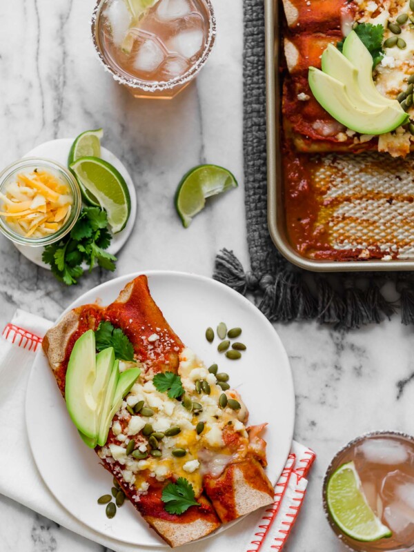 an easy & healthy chicken enchilada recipe perfect for weeknight cooking! these weeknight chicken enchiladas have a filling of pulled chicken, bell pepper sweet onion, black beans, & cheese, and get covered in the easiest blender enchilada sauce made from ancho chiles. the only thing missing is a couple of margaritas! #playswellwithbutter #chickenenchiladas #easychickenenchiladas #enchiladasrecipe #healthyenchiladas #mexicanfoodrecipes #homemadenchiladasauce #enchiladasaucerecipe #easydinnerrecipe #healthydinnerrecipe #mealpreprecipe