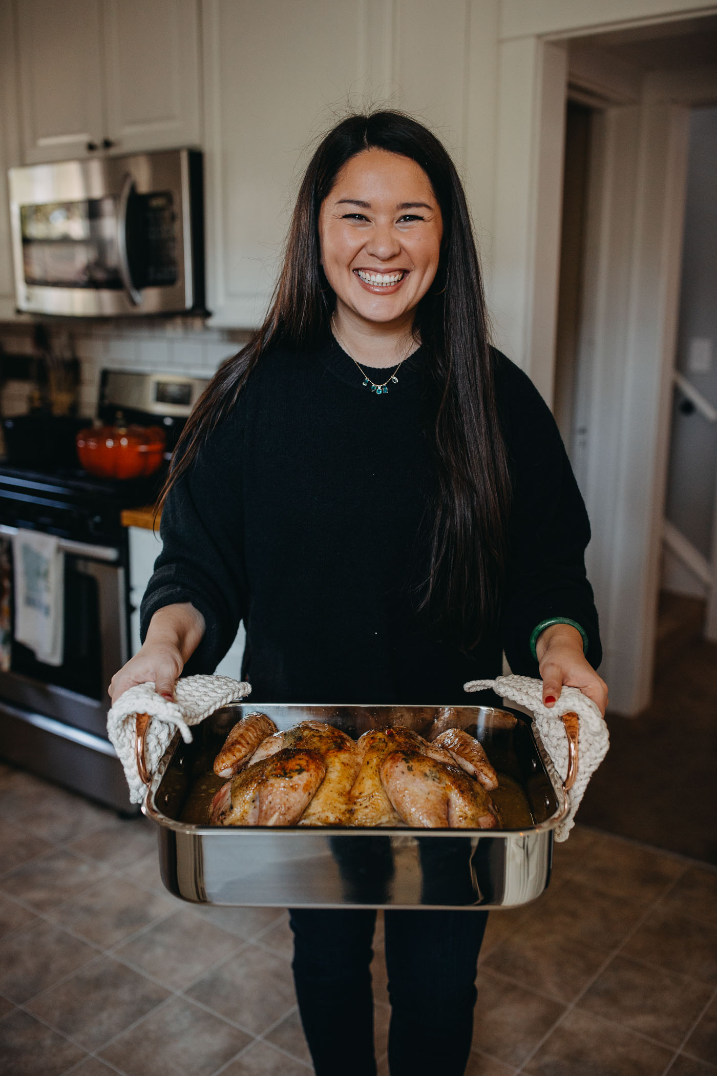 Dark-haired woman in a black sweater holding a roasting dish containing a spatchcocked (butterflied) turkey.