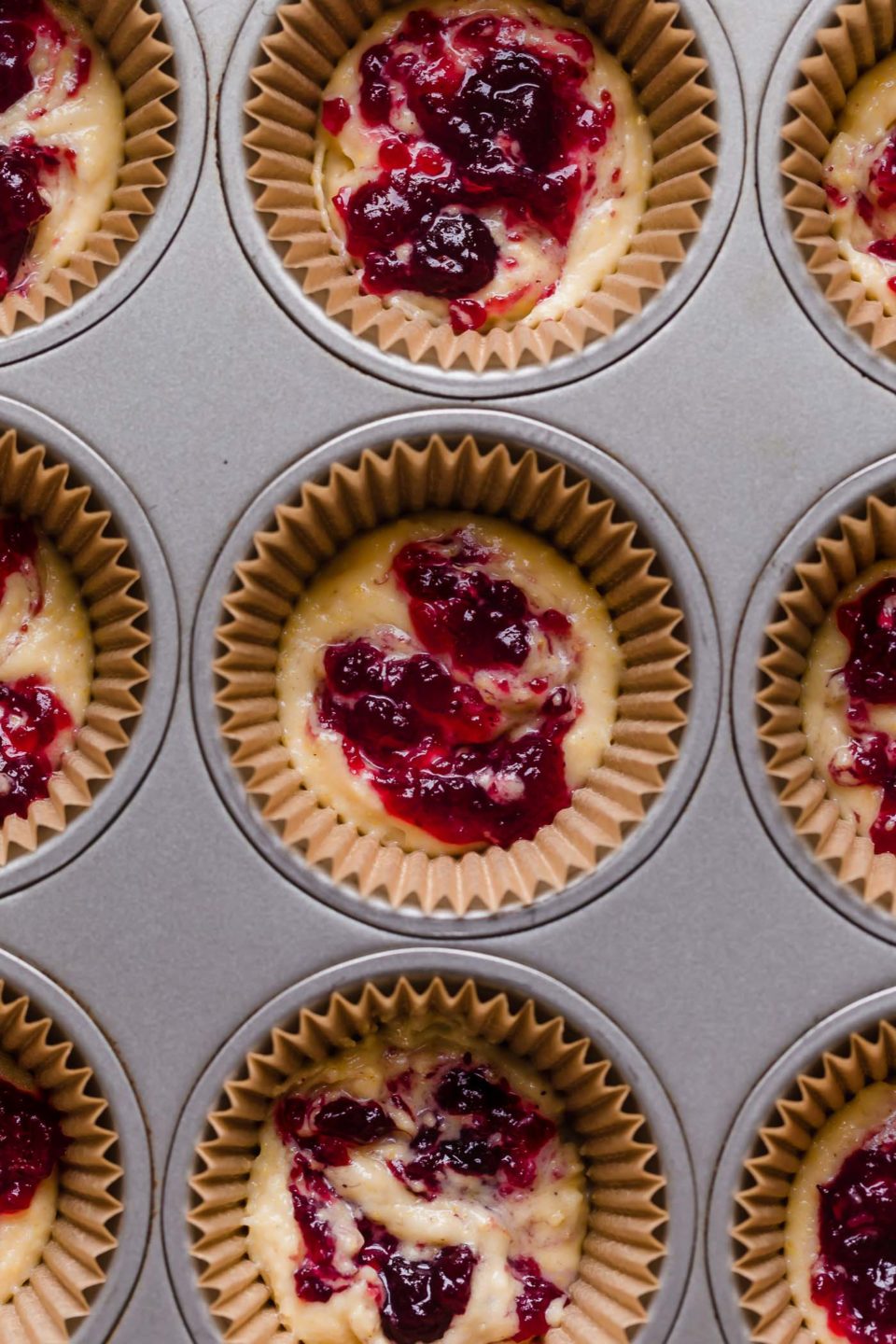 A muffin pan with cranberry sauce swirled into cornbread muffin batter.