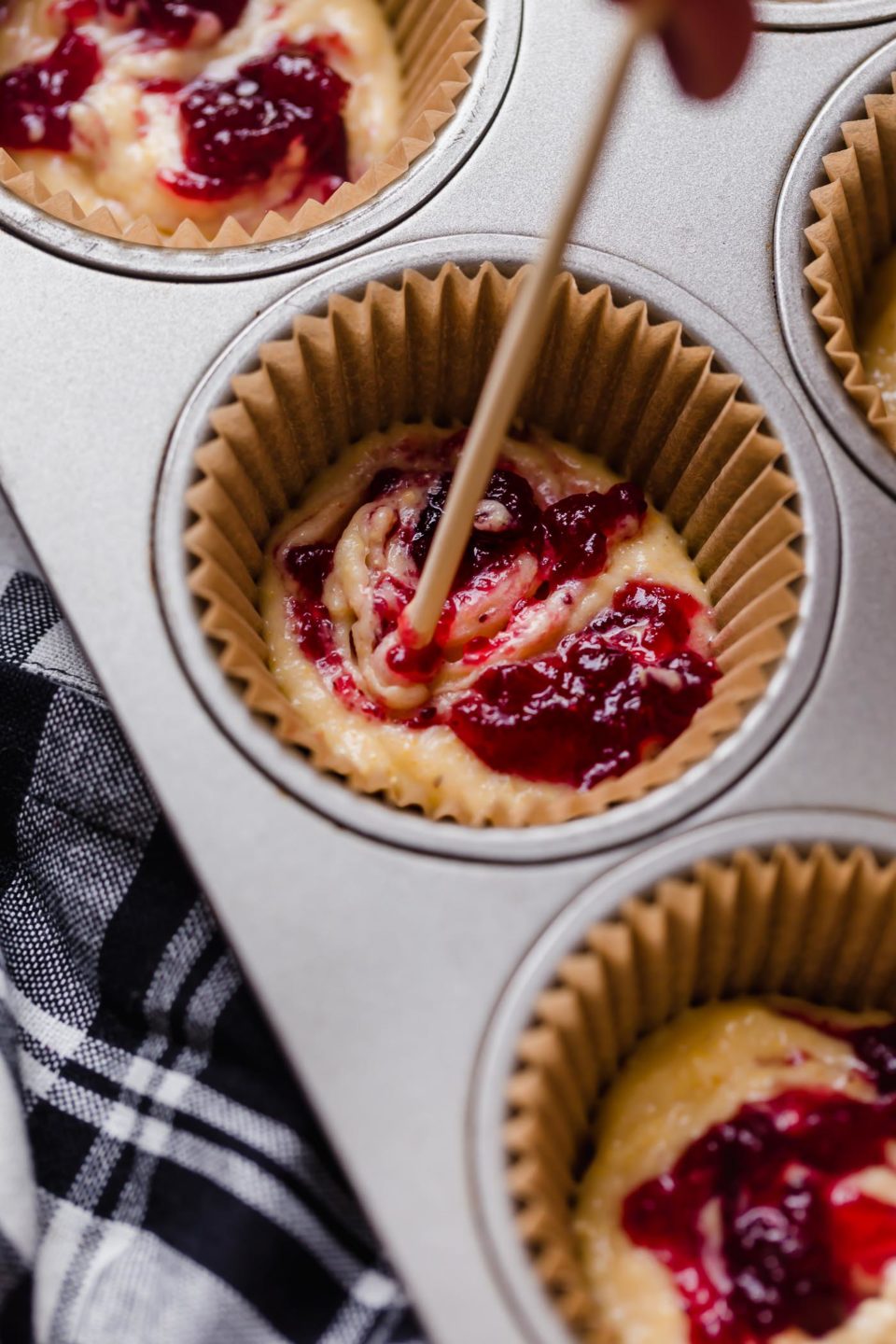 Swirling cranberry sauce into cornbread batter with a toothpick.