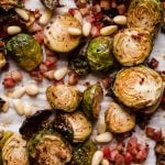Maple roasted brussels sprouts with pancetta & pine nuts arranged on a parchment-lined baking sheet. The brussels sprouts are beautifully golden brown, having been roasted.