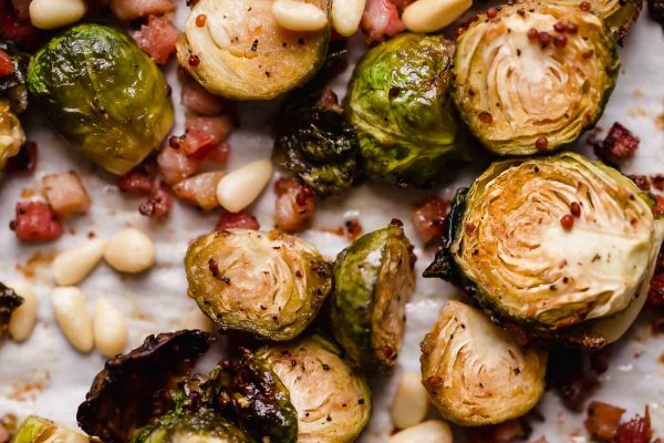 Maple roasted brussels sprouts with pancetta & pine nuts arranged on a parchment-lined baking sheet. The brussels sprouts are beautifully golden brown, having been roasted.