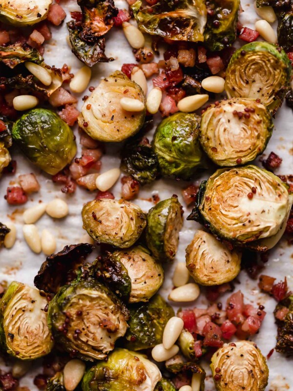 Maple roasted brussels sprouts with pancetta & pine nuts arranged on a parchment-lined baking sheet. The brussels sprouts are beautifully golden brown, having been roasted.
