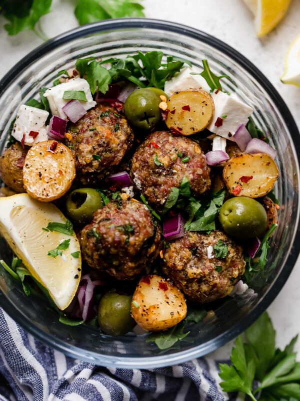 the easiest juicy & tender baked lamb meatballs, made with panko breadcrumbs, lemon, parsley, oregano & cumin, served on top of a seriously healthy meal prep bowl with lemony Greek roasted potatoes, greens, feta, olives, & homemade Romesco sauce. an easy & satisfying meal prep recipe for lunches all week long! #playswellwithbutter #lambmeatballs #bakedlambmeatballs #greeklambmeatballs #groundlamb #mealpreprecipes #mealpreprecipesfortheweek #mediterraneandiet #healthybowlsrecipe