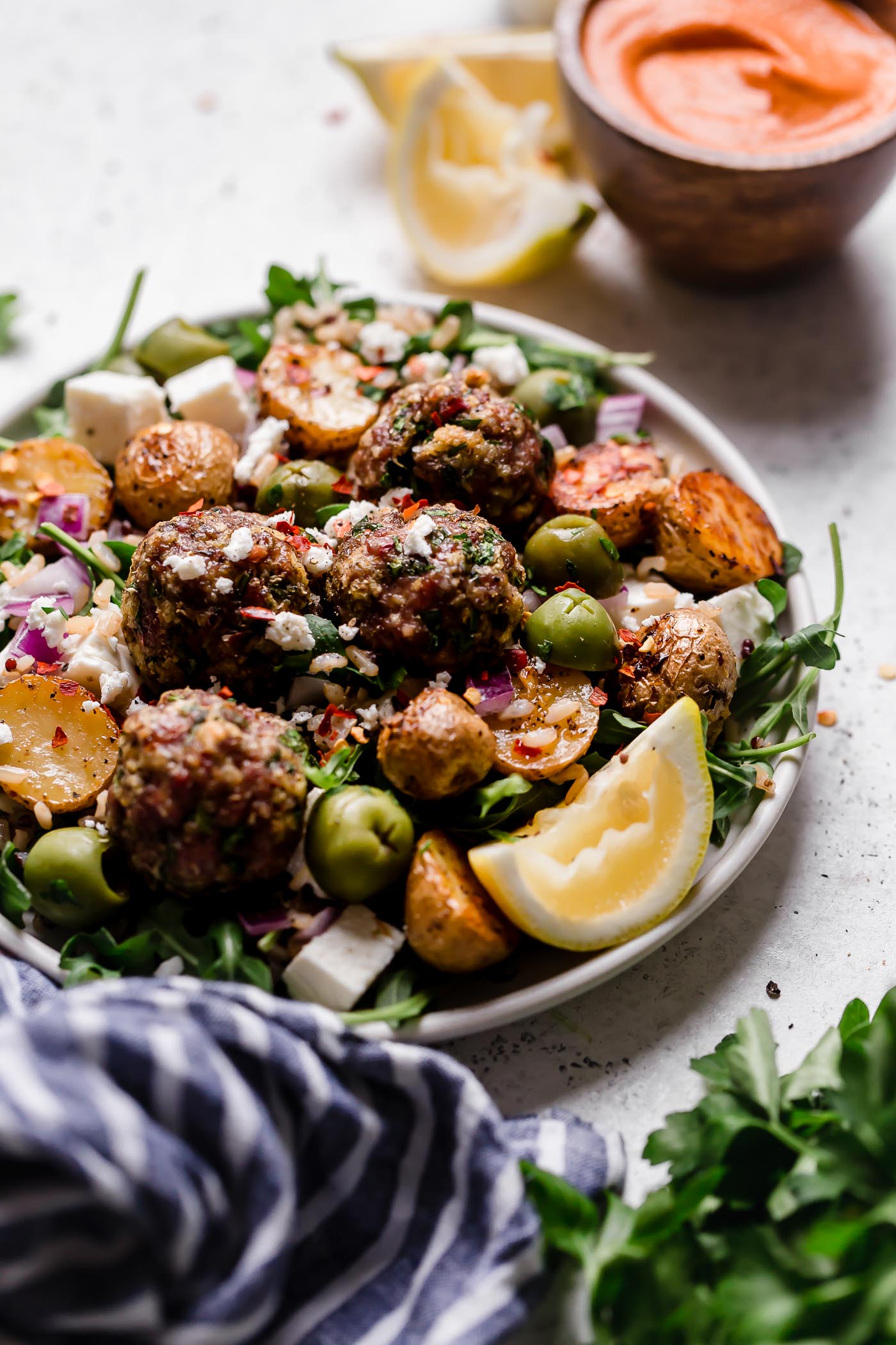 the easiest juicy & tender baked lamb meatballs, made with panko breadcrumbs, lemon, parsley, oregano & cumin, served on top of a seriously healthy meal prep bowl with lemony Greek roasted potatoes, greens, feta, olives, & homemade Romesco sauce. an easy & satisfying meal prep recipe for lunches all week long! #playswellwithbutter #lambmeatballs #bakedlambmeatballs #greeklambmeatballs #groundlamb #mealpreprecipes #mealpreprecipesfortheweek #mediterraneandiet #healthybowlsrecipe