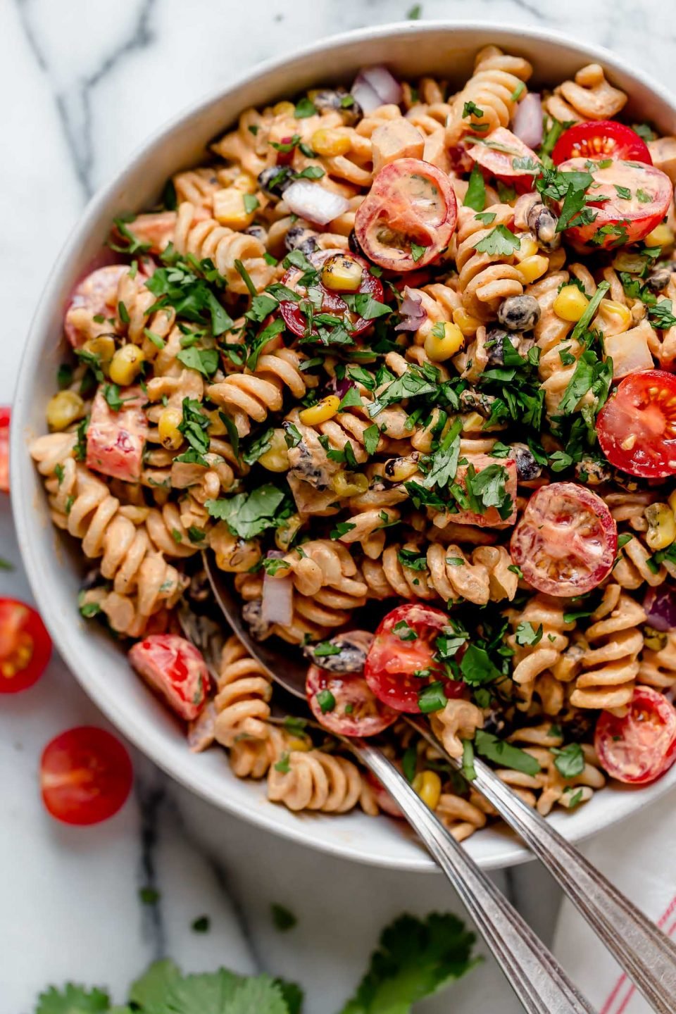 Vegan southwest pasta salad in a white bowl, served with 2 large serving spoons.
