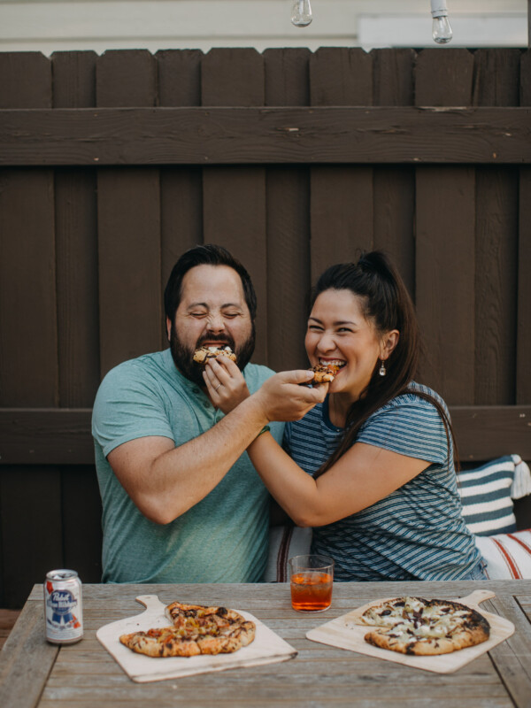 man & woman enjoying pizza night on a deck, feeding each other homemade pizza!