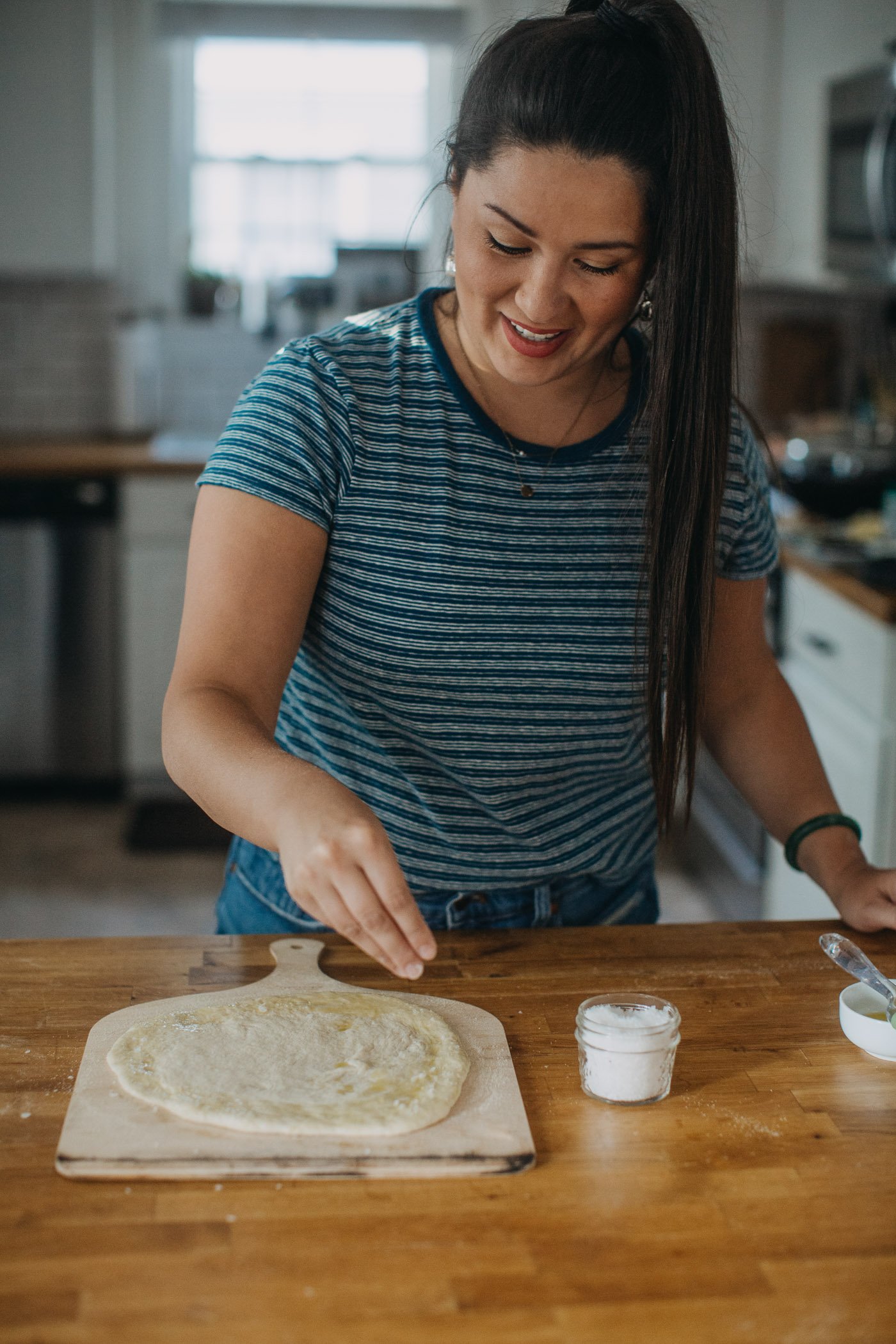Woman in blue shirt sharing favorite pizza dough tip for pizza night: sprinkle salt on the edge of the crust!