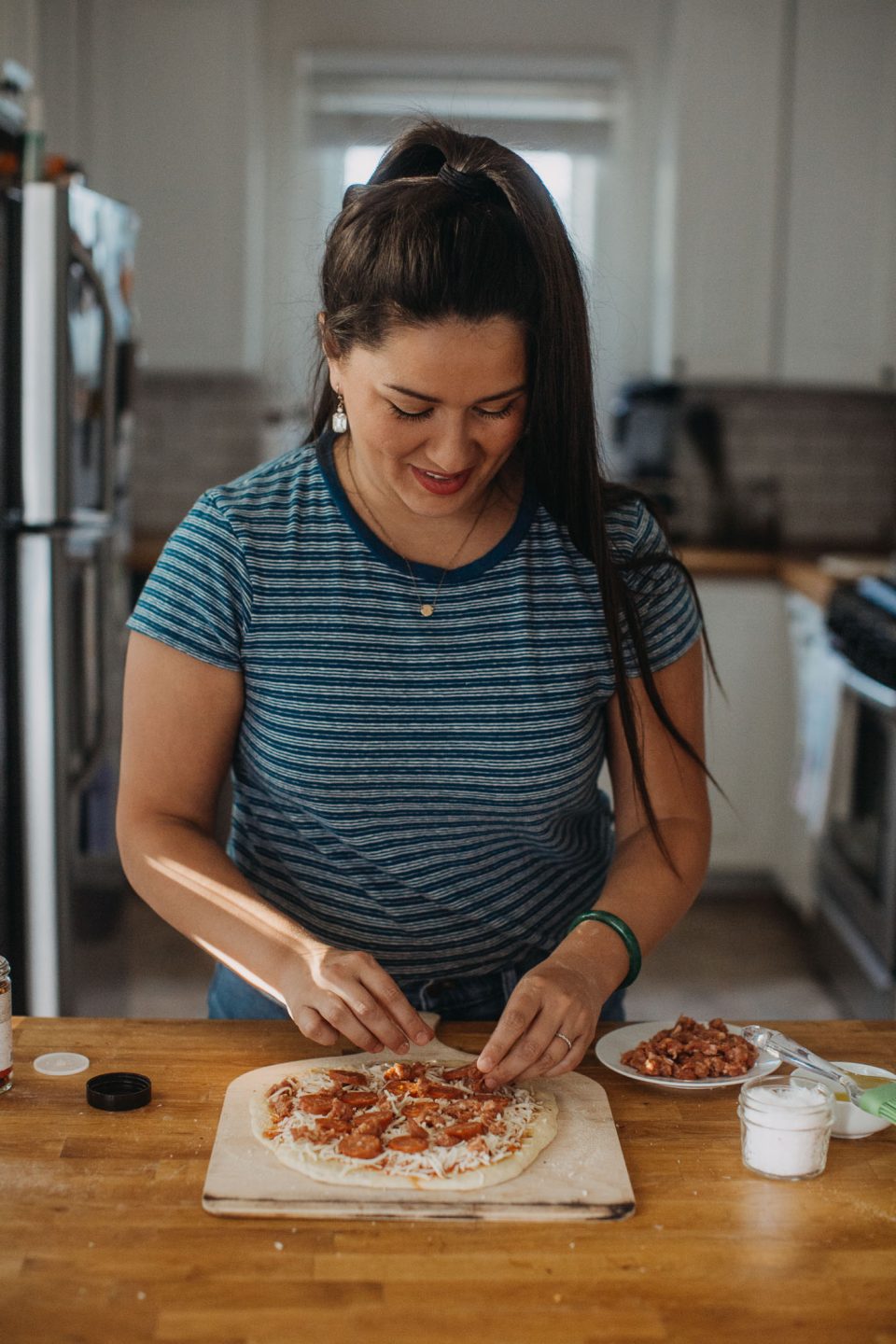 woman in blue shirt showing how to make homemade pizza for pizza night by adding fresh sausage to pizza.
