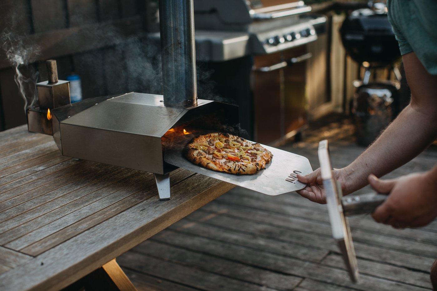 hand transferring homemade pizza from a pizza peel to an Ooni pizza oven (model: Ooni 3)