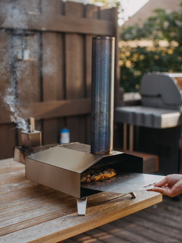 hand transferring homemade pizza from a pizza peel to an Ooni pizza oven (model: Ooni 3)
