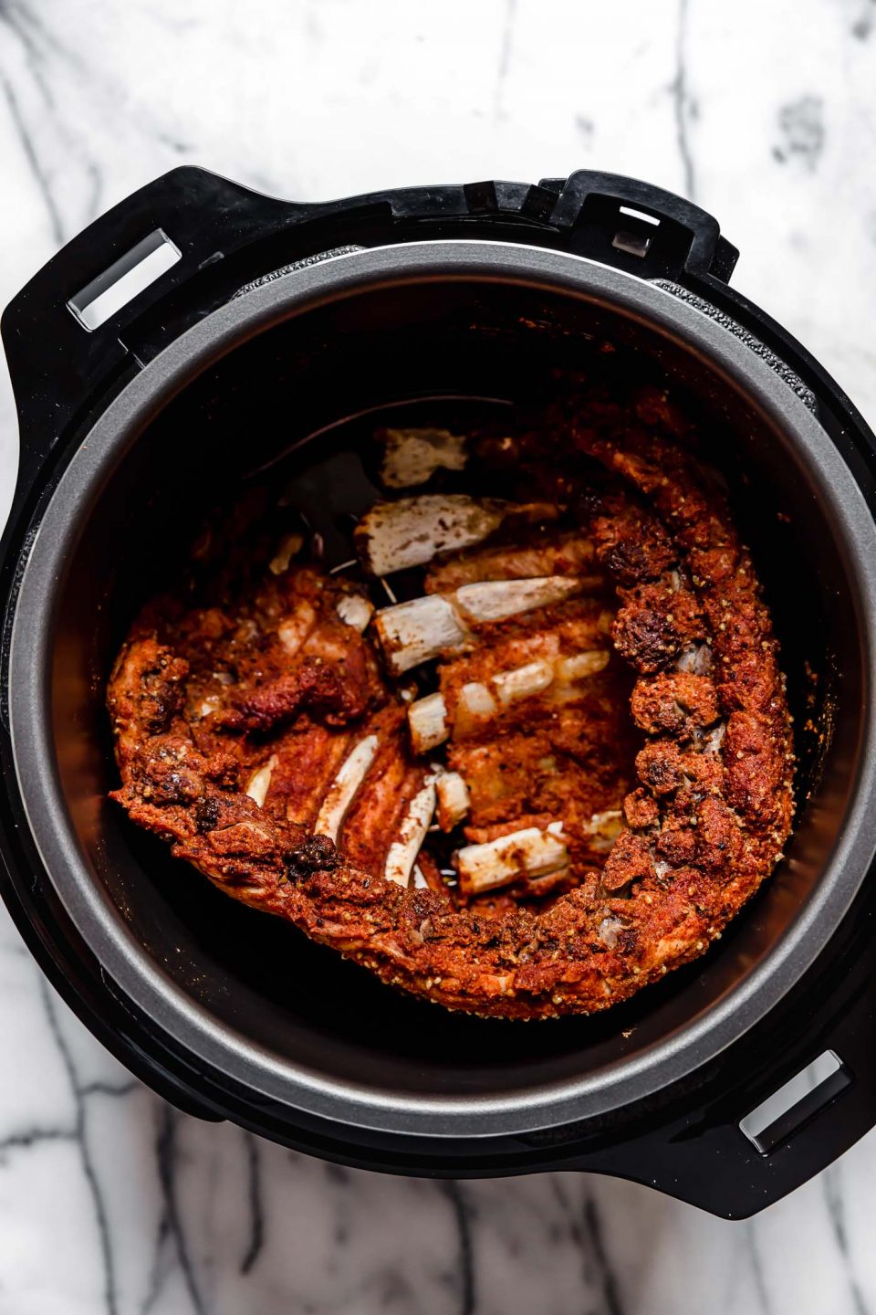 Seasoned ribs shown in electric pressure cooker after cooking.