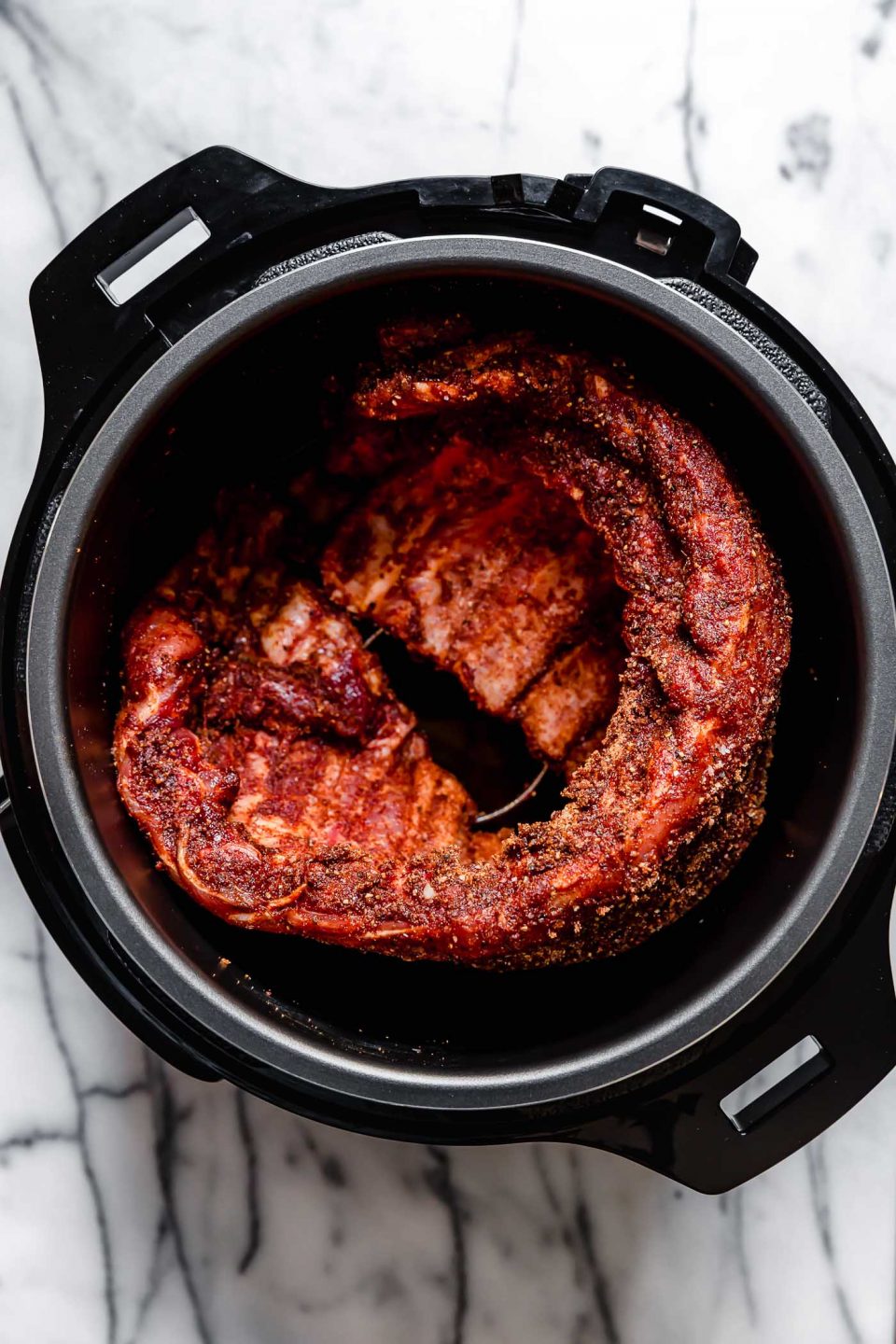 Seasoned ribs shown in electric pressure cooker prior to cooking.