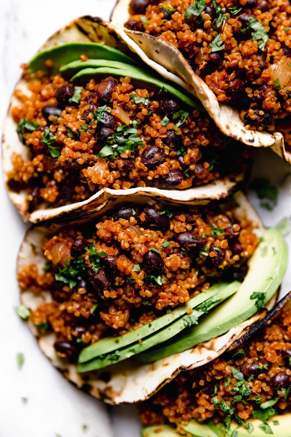 Black Bean Quinoa Tacos arranged on a marble board, topped with chopped cilantro.