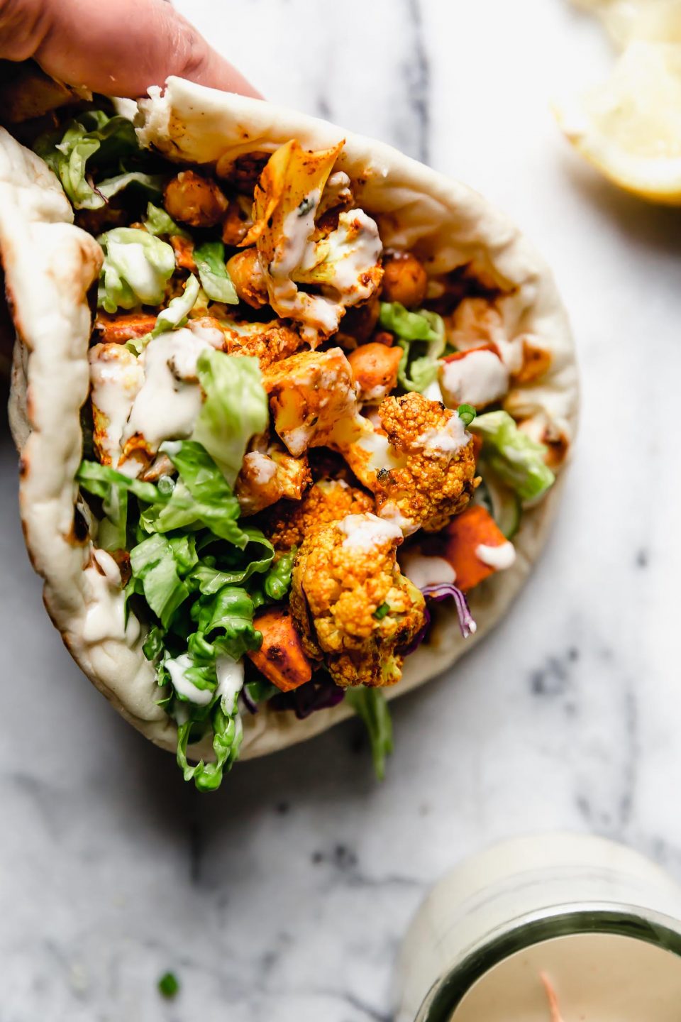 Vegetarian shawarma served in a pita, topped with a drizzle of tahini sauce. A woman's hands are reaching into the frame of the photo, holding the sandwich.