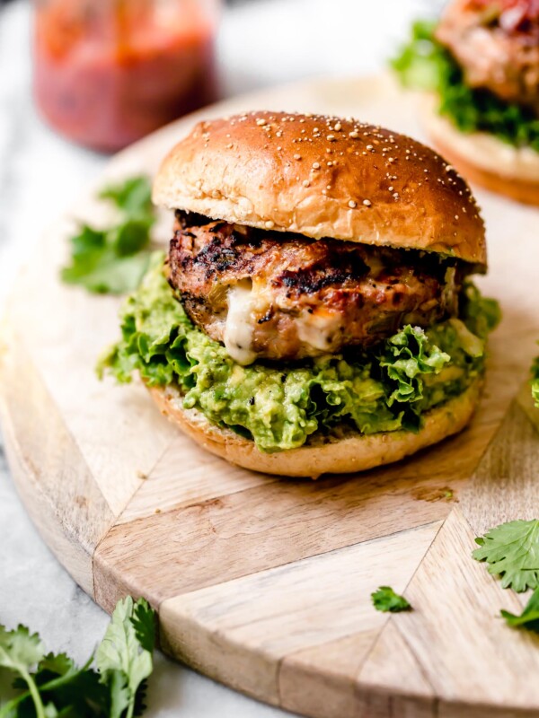 Stuffed Southwest Turkey Burger place on a burger bun with lettuce & guacamole. Burger is sitting on a light wood board, with a jar of salsa behind it.