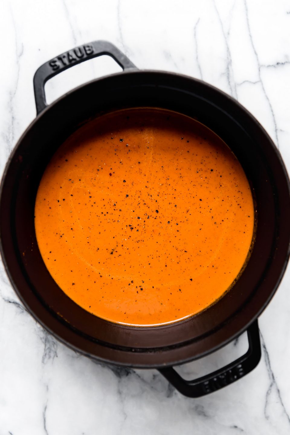 Creamy Roasted Red Pepper Soup, blended & topped with cracked black pepper, in a black Staub dutch oven.
