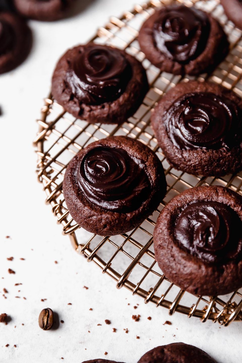 Double chocolate thumbprint cookies arranged on a copper wire baking rack, a top a white surface.