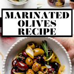 Homemade marinated olives served in a white dish with scalloped edges. The bowl is atop a copper wire rack on a white surface, surrounded by fresh rosemary, lemon peel, a small wooden bowl with red chili flakes, & a couple glasses of red wine.