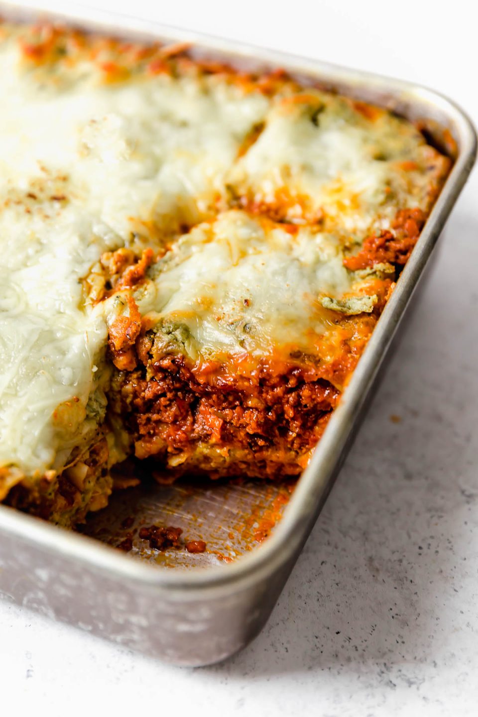 Christmas Eve Lasagna in a baking dish, showing the layers of bolognese sauce, pesto, pasta & cheese.