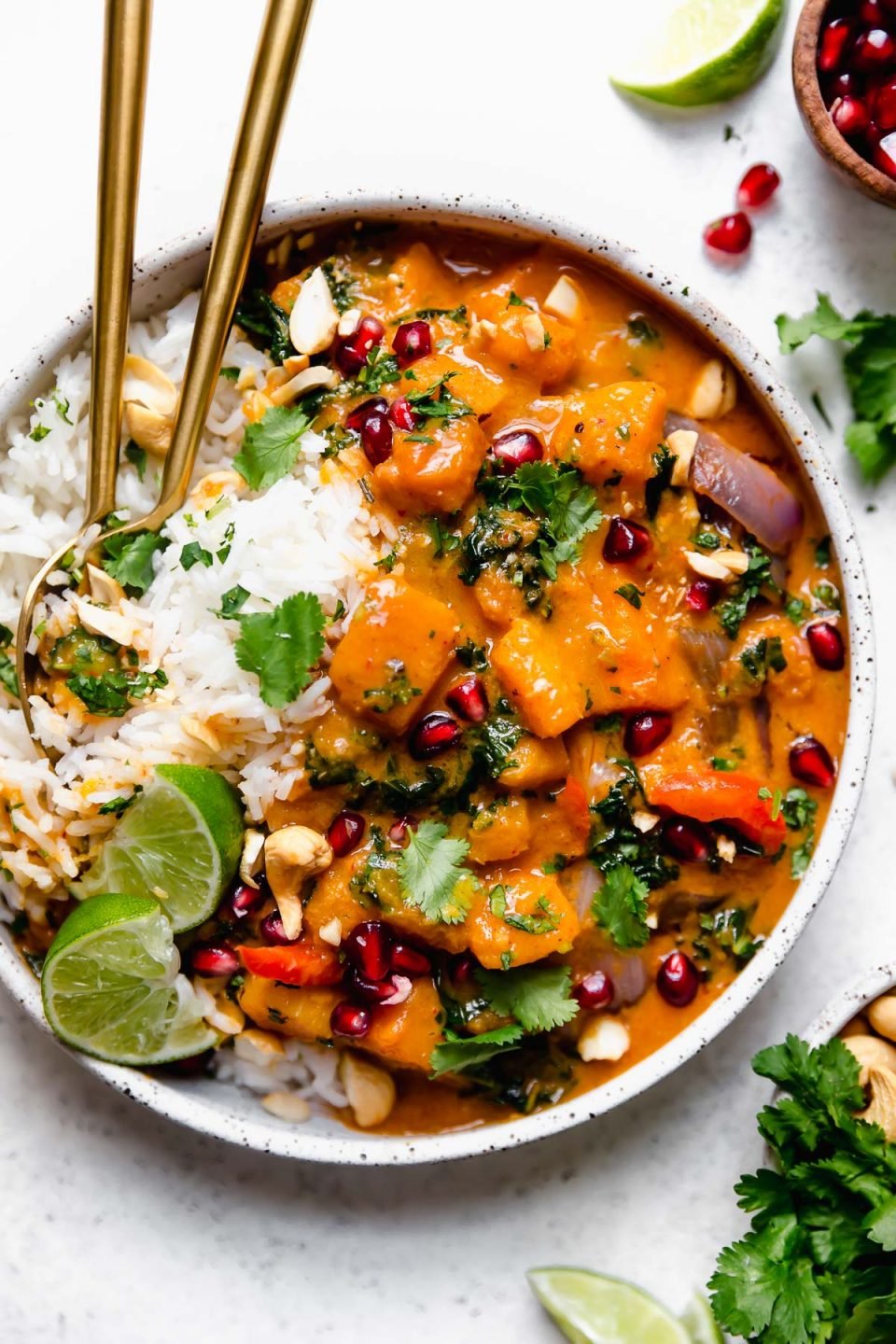 Butternut Squash Red Curry in a speckled white bowl, with white rice, chopped cilantro, cashews, & pomegranate arils.