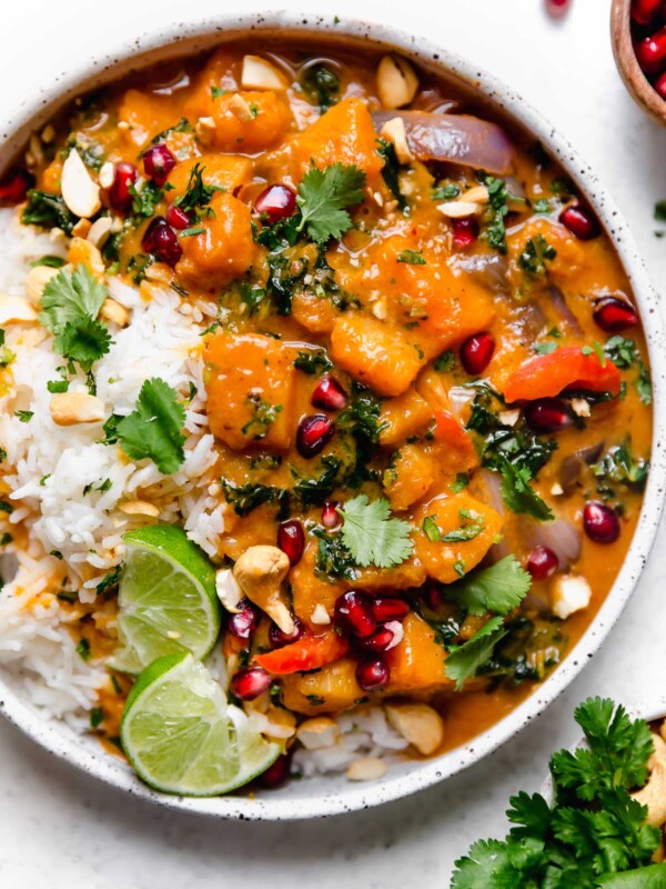 Butternut Squash Red Curry in a speckled white bowl, with white rice, chopped cilantro, cashews, & pomegranate arils.