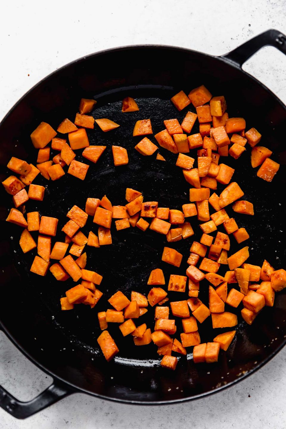 How to make chorizo and potato tacos - Step 1: Sweet Potatoes browning in a large skillet atop a white background.