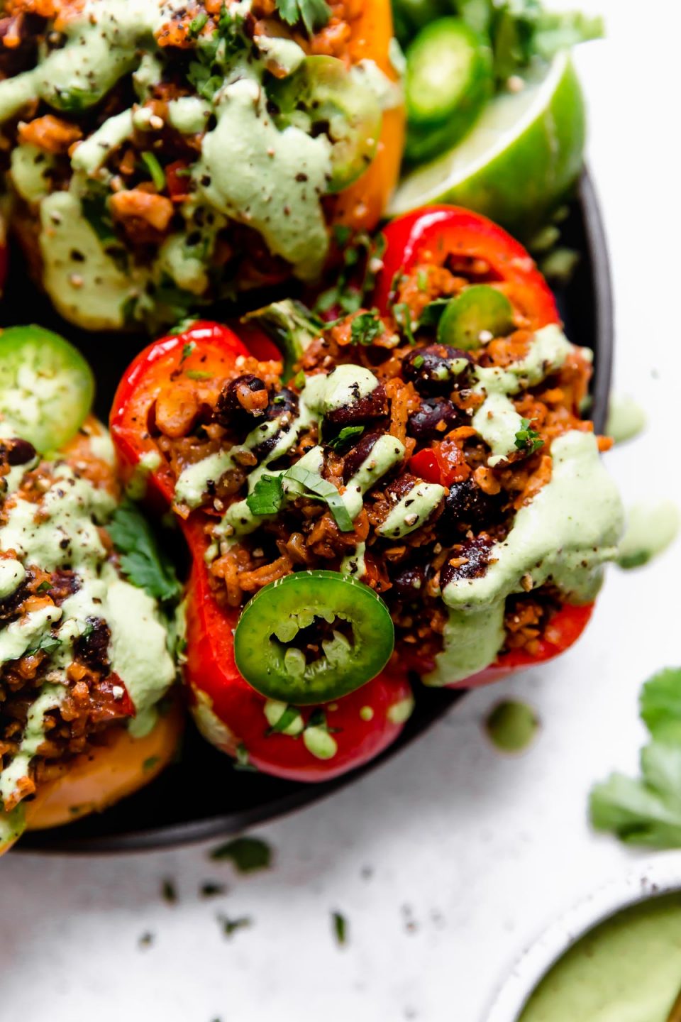 Close up photo of a vegan stuffed peppers on a small black plate, topped with cilantro lime cashew crema, sliced jalapenos, & chopped cilantro. 