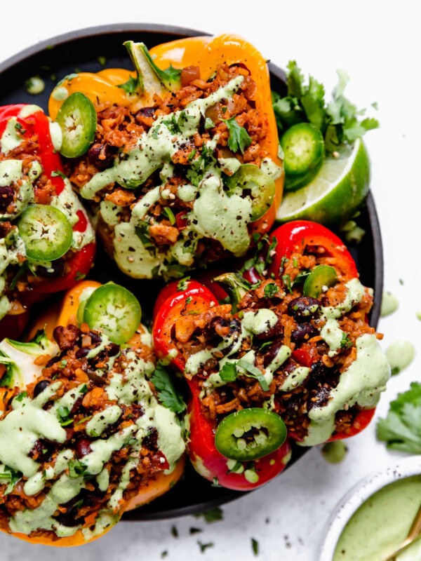 4 Vegan Stuffed Peppers on a small black plate, topped with cilantro lime cashew crema, sliced jalapenos, lime wedges & cilantro.