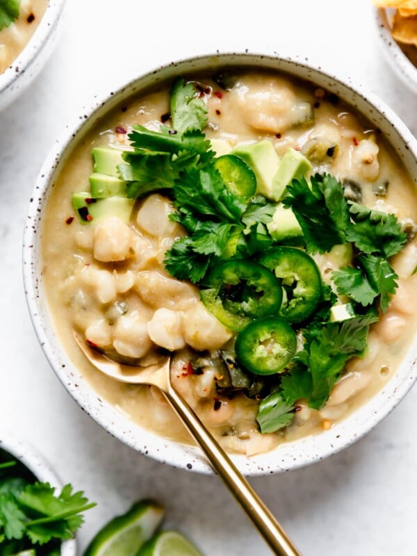 Vegan white chili served in a speckled ceramic bowl, topped with sliced jalapeno, cilantro, & diced avocado.