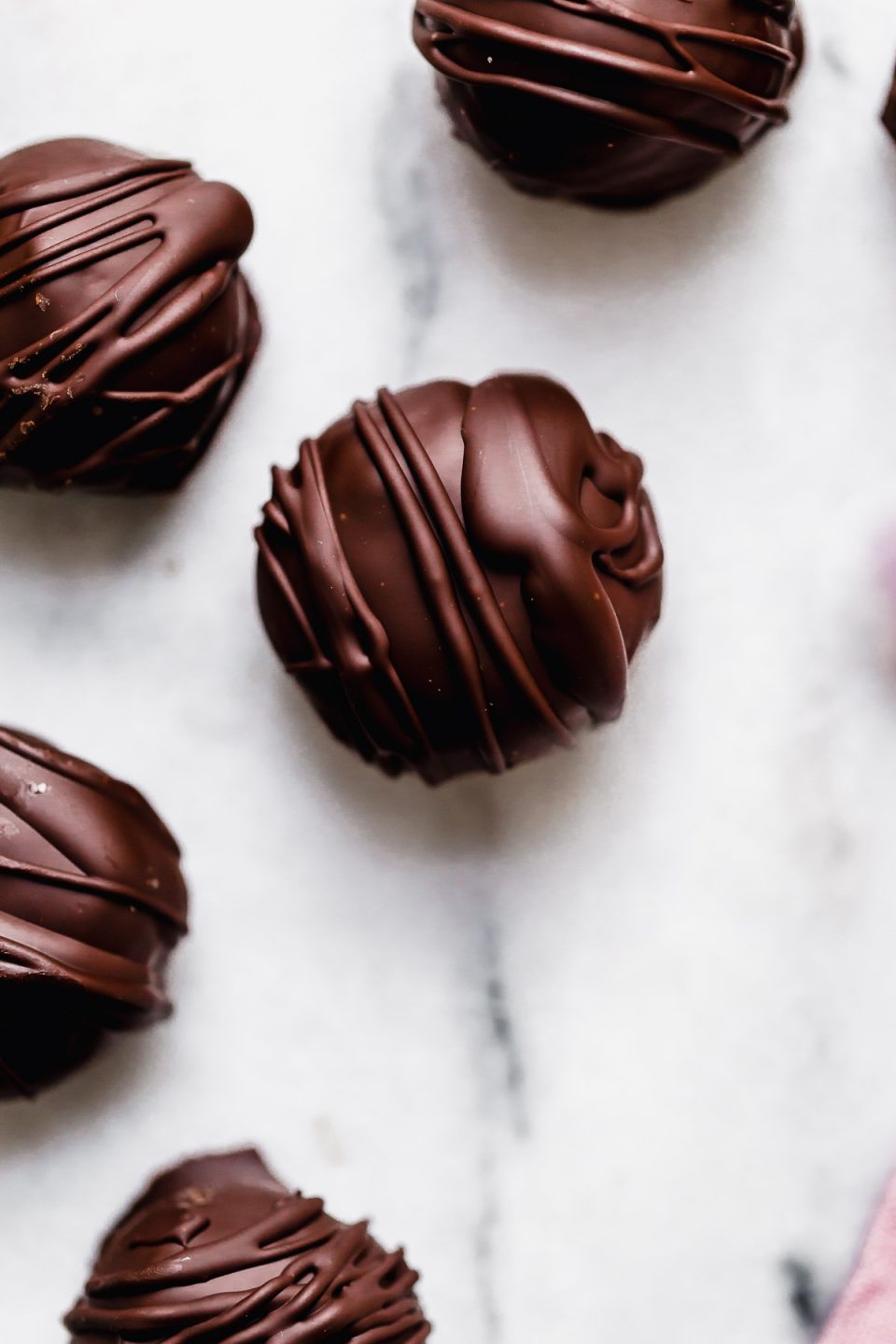Chocolate-covered vegan cookie dough bites on a white, marble surface.
