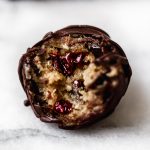Chocolate-covered vegan cookie dough bite sitting on a white surface. A bite has been taken out of the ball, revealing an inside studded with ruby-red Montmorency tart cherries.