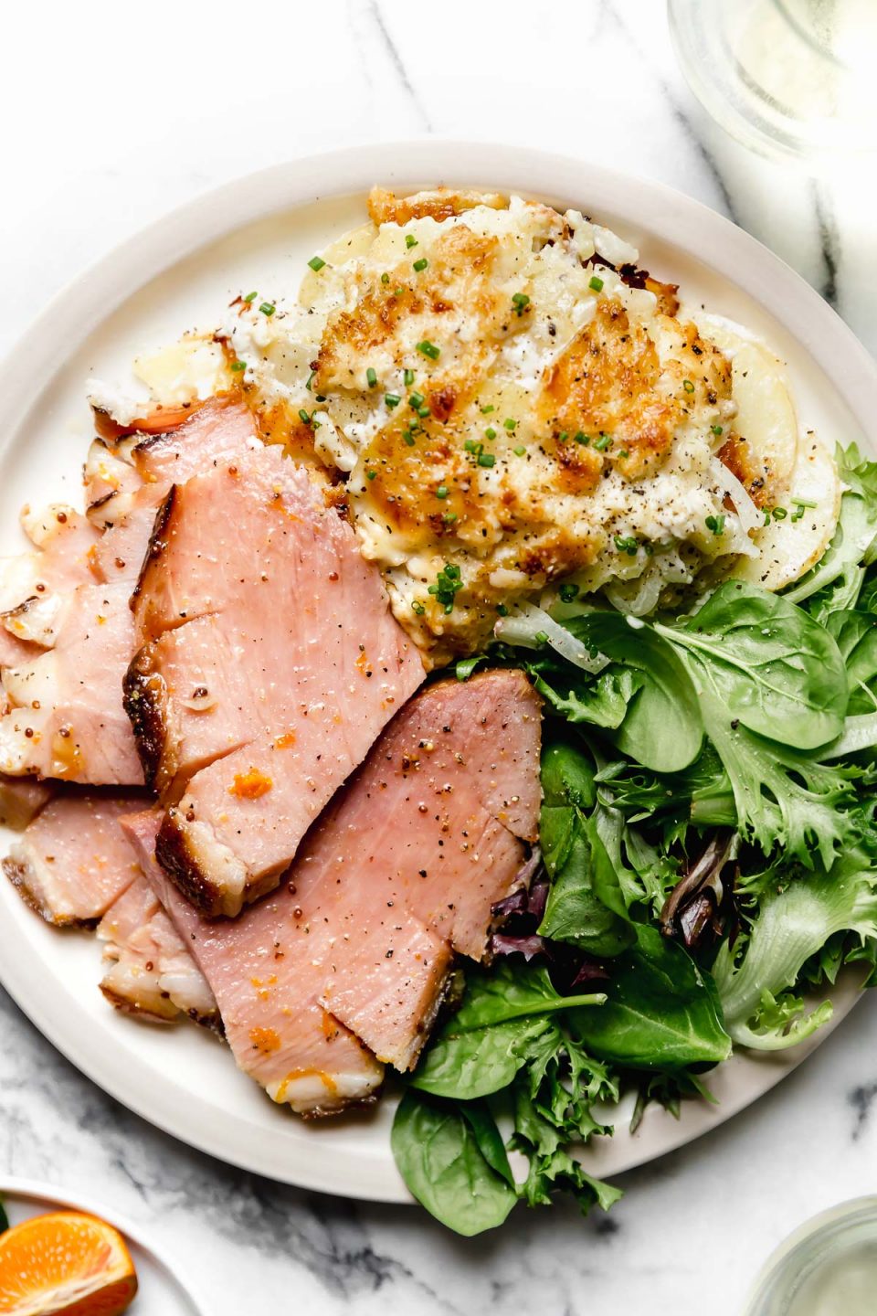 Thick slices maple glazed baked ham, plated on a dinner plate with greens & au gratin potatoes.