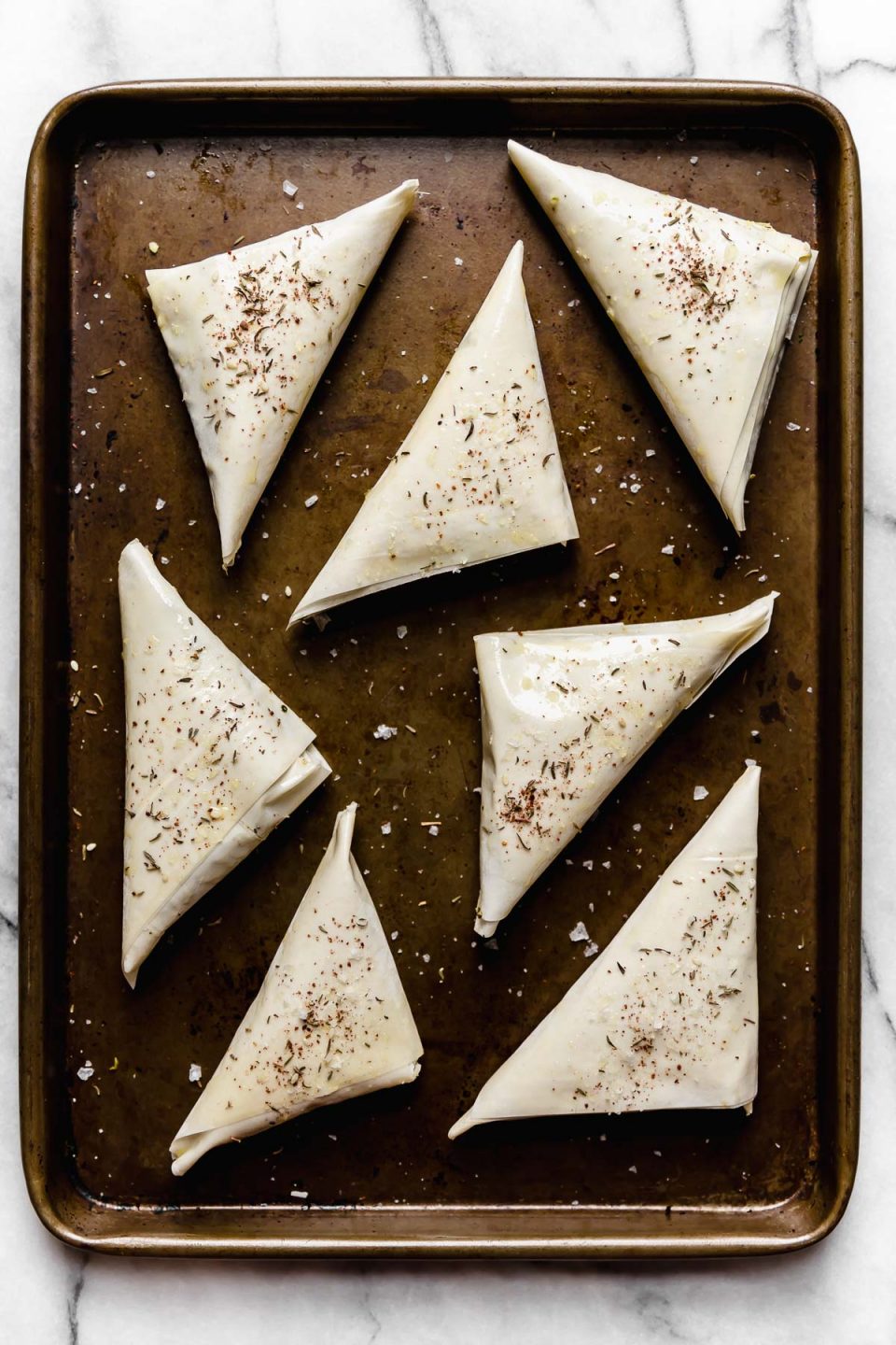 Unbaked spanakopita triangles arranged on a baking sheet.