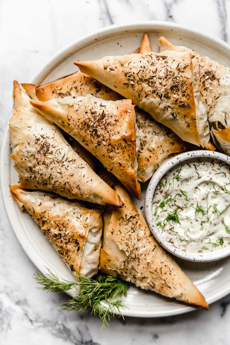 Baked Spanakopita Triangles on a plate with tzatziki dipping sauce.