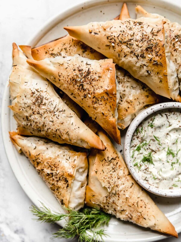 Baked Spanakopita Triangles on a plate with tzatziki sauce.