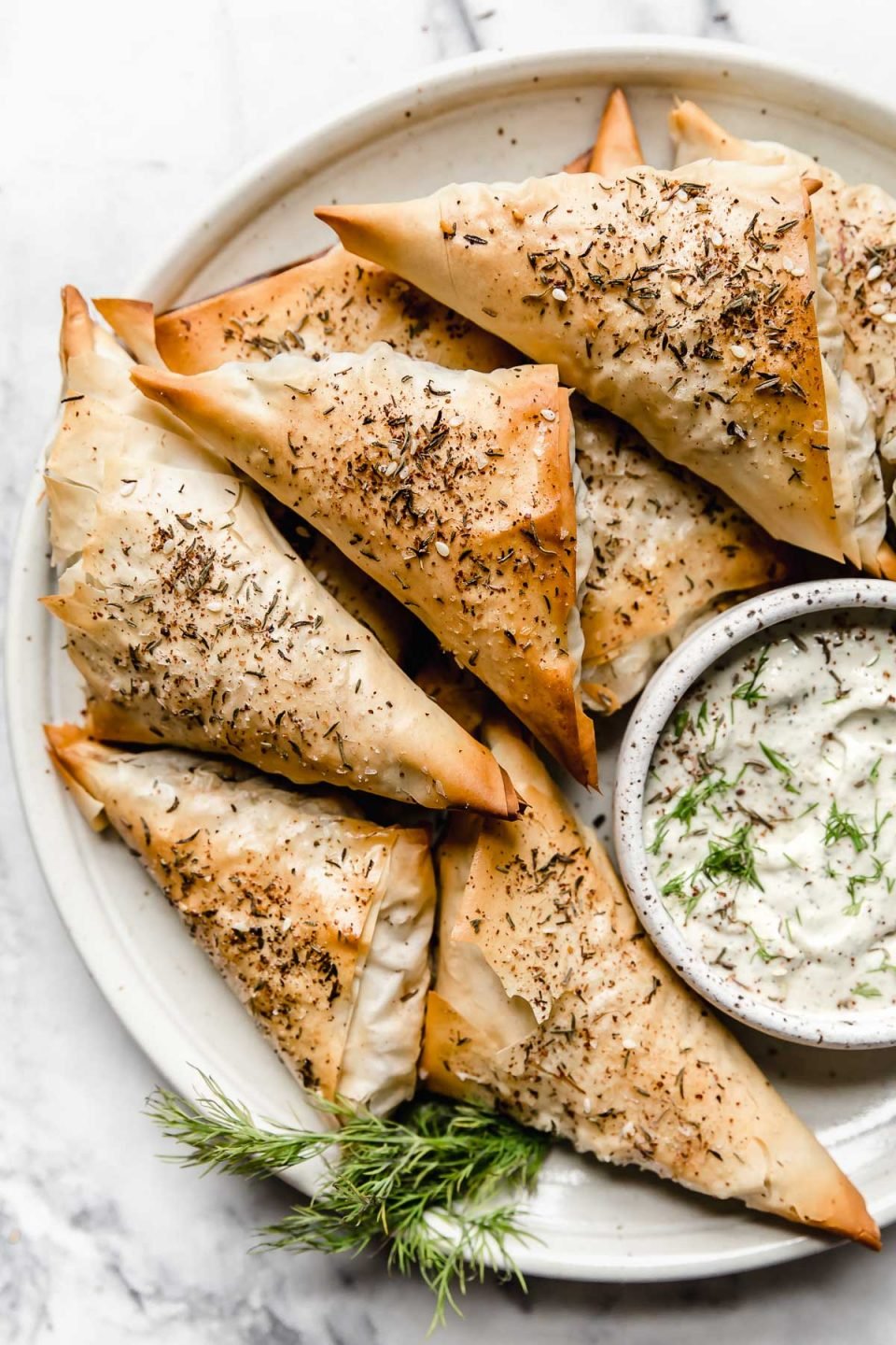 Baked Spanakopita Triangles on a plate with tzatziki sauce.