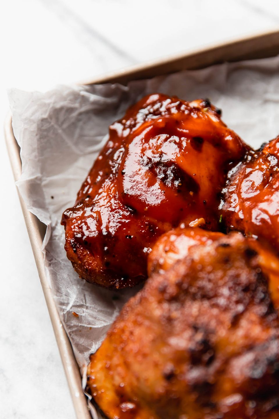 Close up of a grilled barbecue chicken thigh slathered in BBQ sauce.