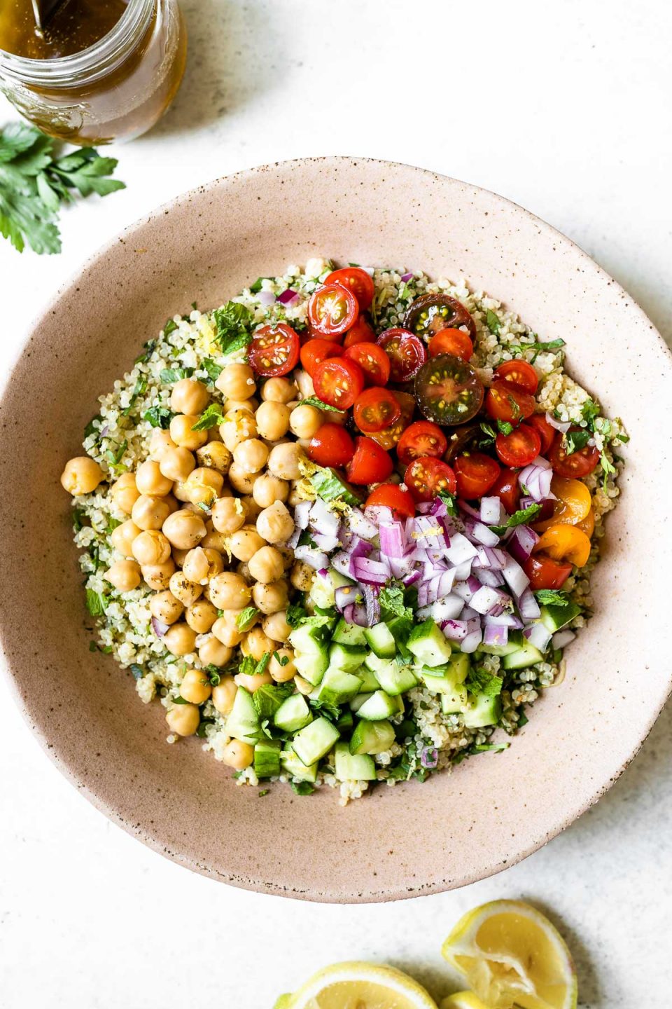 Falafel-ish quinoa salad ingredients layered in groups in a large pink serving dish - quinoa topped with chickpeas, cucumbers, diced red onion & tomatoes.