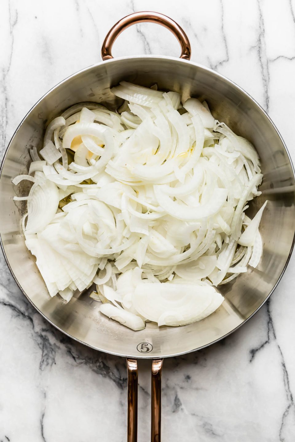Thinly sliced yellow onion in a large pan before caramelizing.