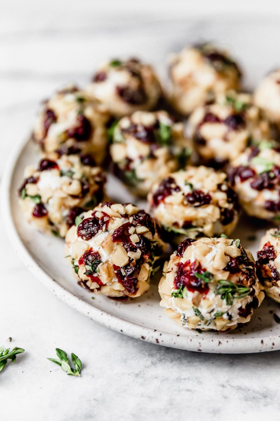 Herbed goat cheese balls, coated in chopped nuts & tart cherries, on a small, speckled white plate.