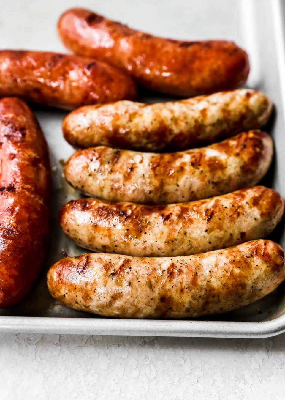 Grilled sausage links are arranged atop a parchment lined baking sheet.