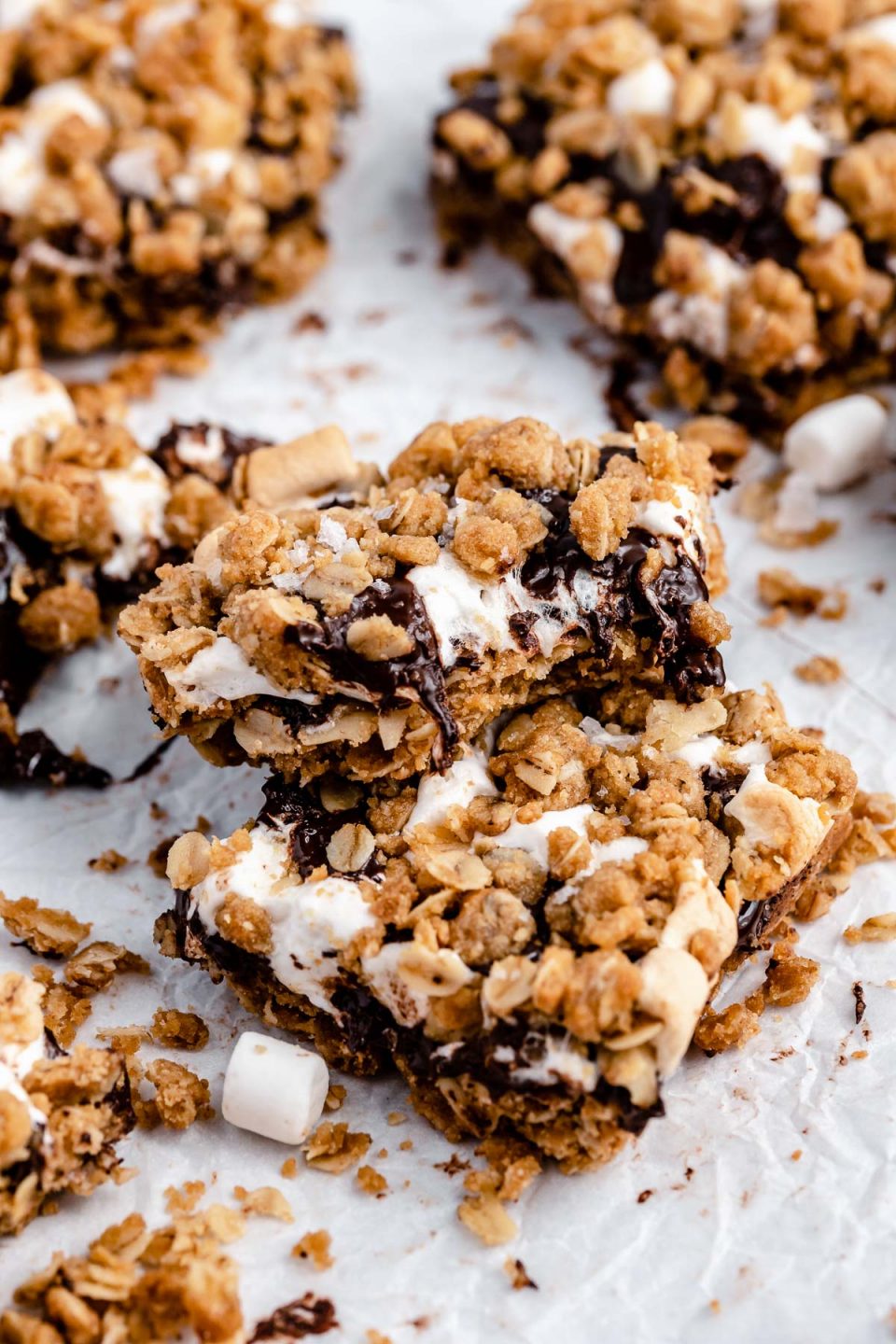 A stack of 3 gooey s'mores crumble bars, surrounded by mini marshmallows and additional bars.