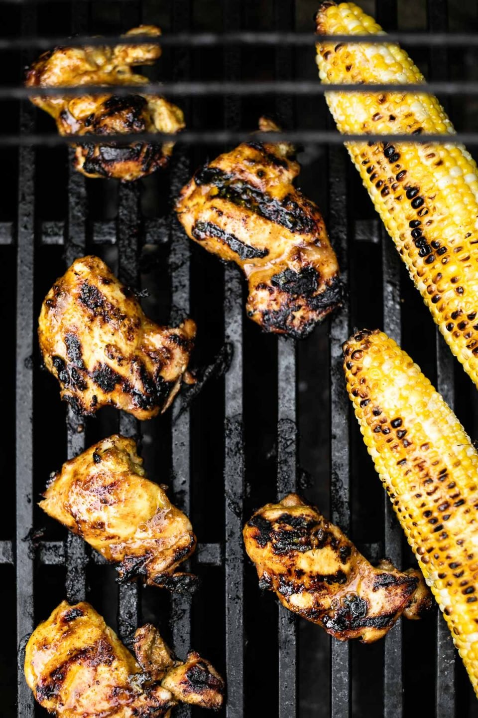 Curry marinated chicken & corn on the cob shown grilling on grill grates.